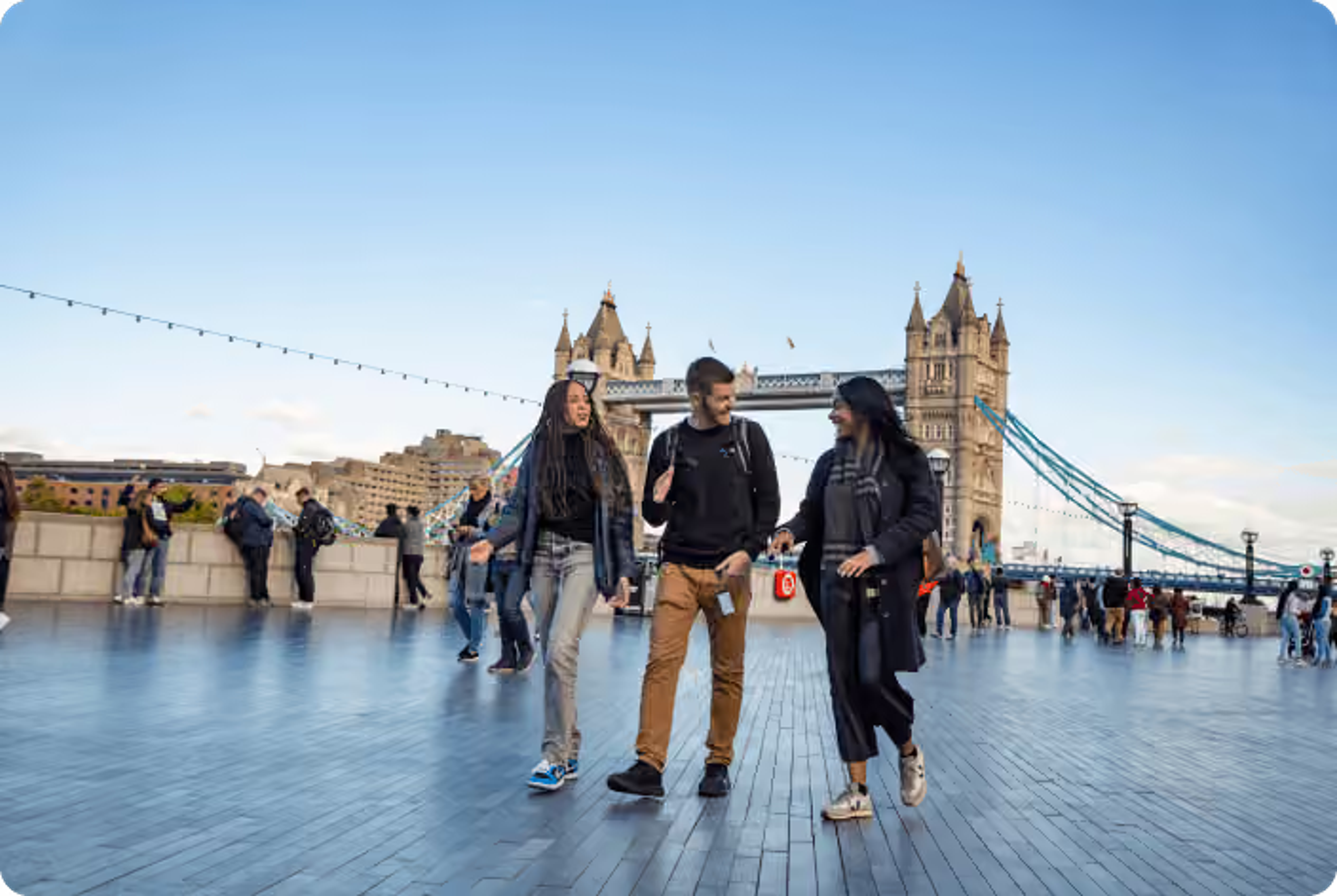 Three colleagues walking and talking along a waterfront, with the London Tower Bridge in the background