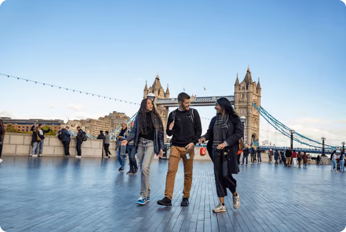 Three colleagues walking and talking along a waterfront, with the London Tower Bridge in the background
