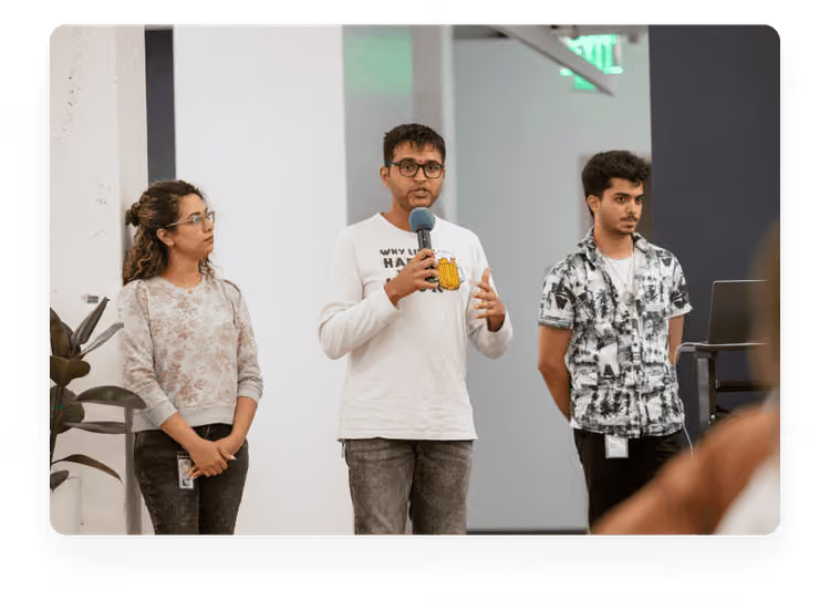 Three young colleagues standing together in a modern office space, with the person in the center speaking into a microphone