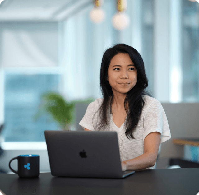 A young woman sitting at a desk with an open laptop in a bright, modern office setting
