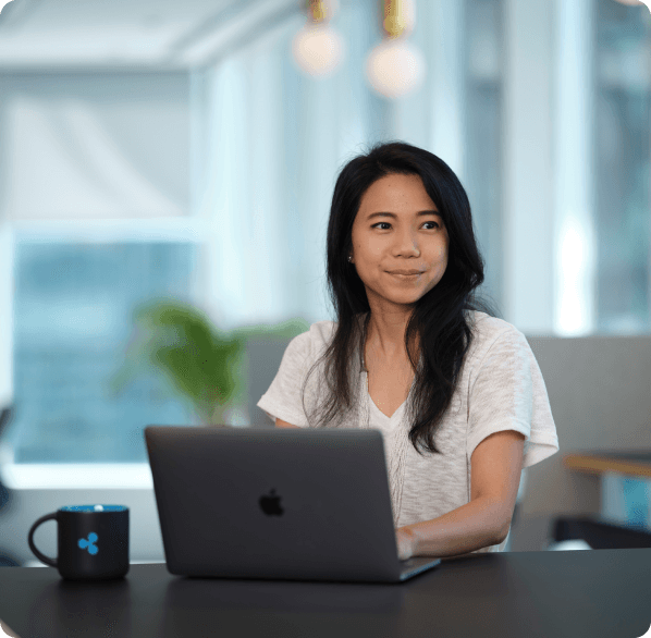 A young woman sitting at a desk with an open laptop in a bright, modern office setting