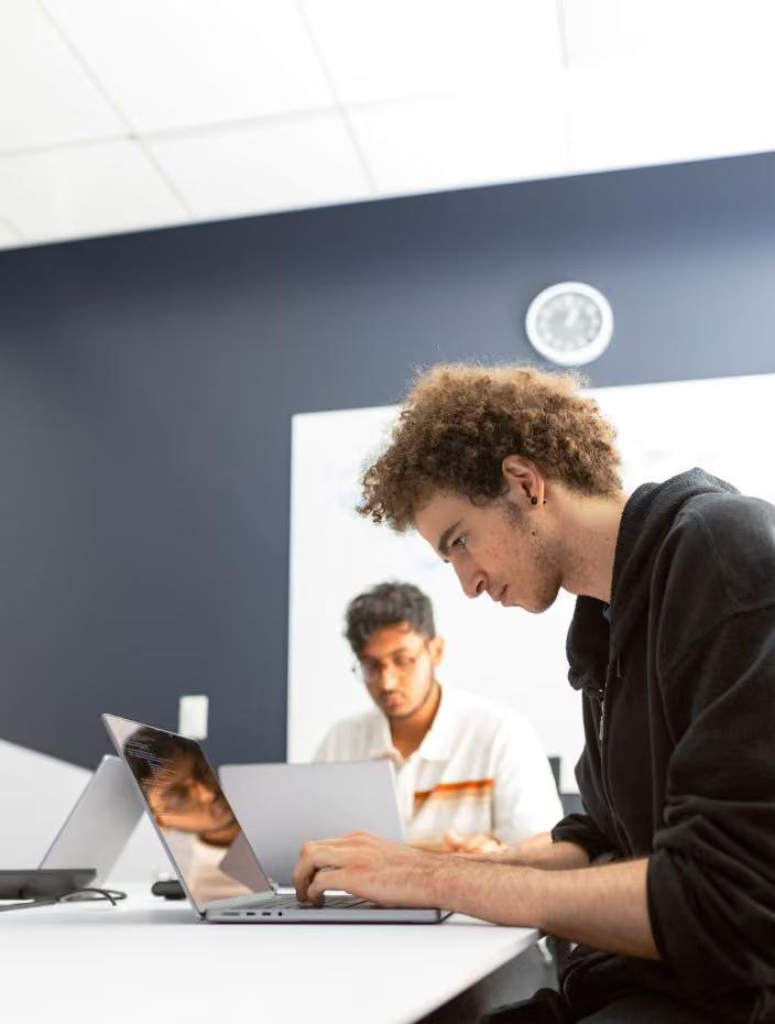 Two young men working on laptops at a desk in a bright office setting