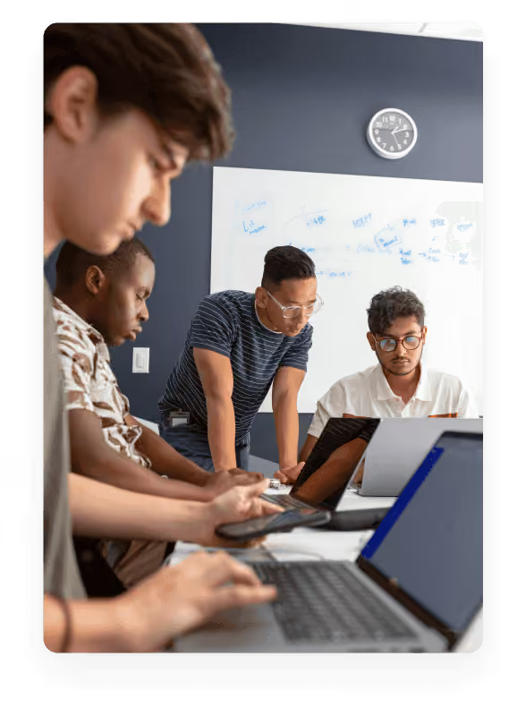Three young men collaborating over laptops at a desk in a bright, modern office setting