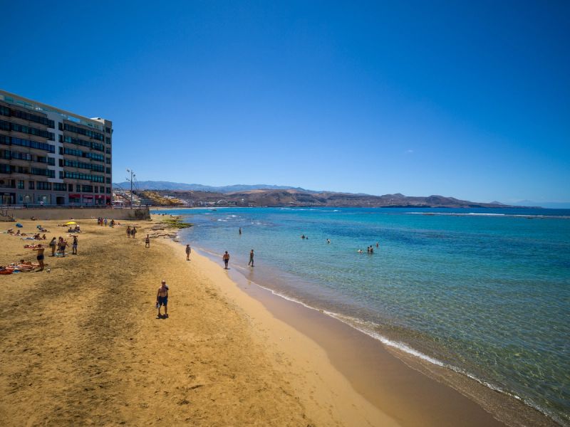 Sunny day at Playa de Las Canteras with golden sand, clear turquoise water, and beachfront apartments