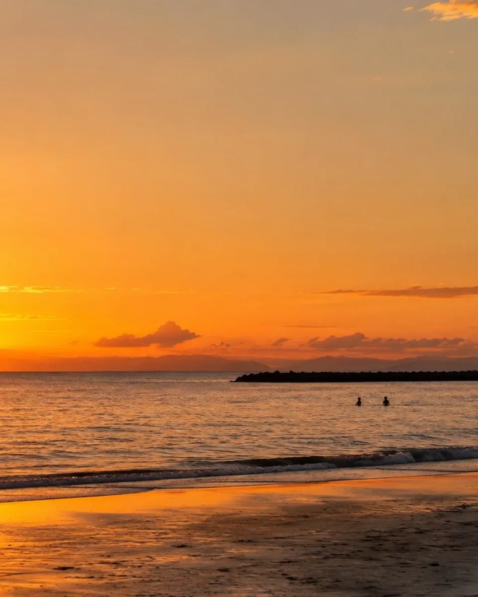 A couple walking hand in hand on Las Canteras beach at sunset, with golden light reflecting on the water.