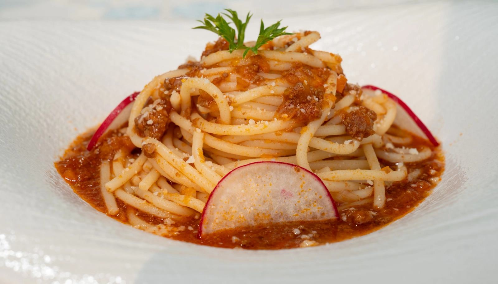 Close-up of pasta in a red sauce with a thin radish garnish.