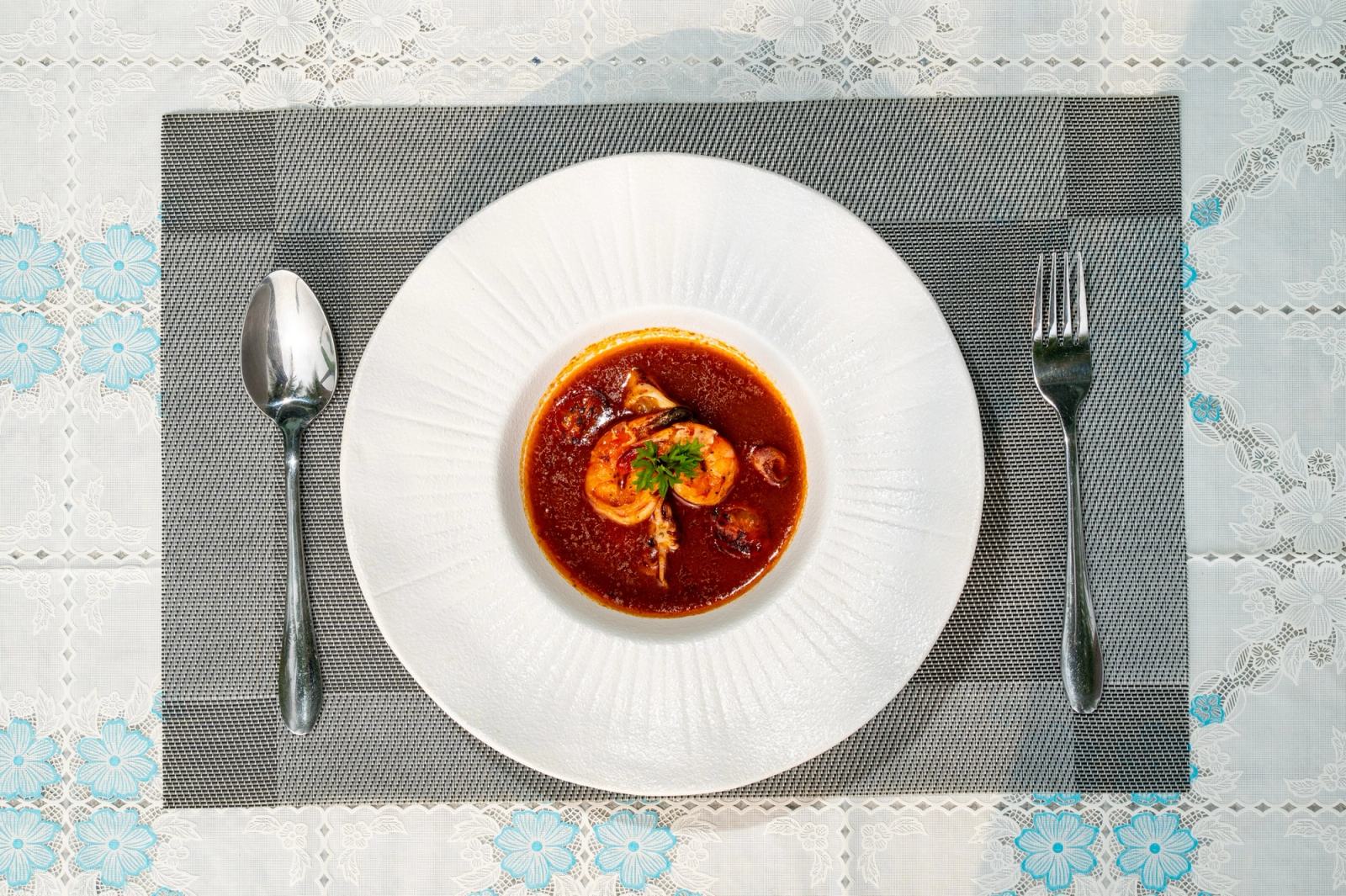 Red soup with a green garnish in a wide white bowl, viewed from above.