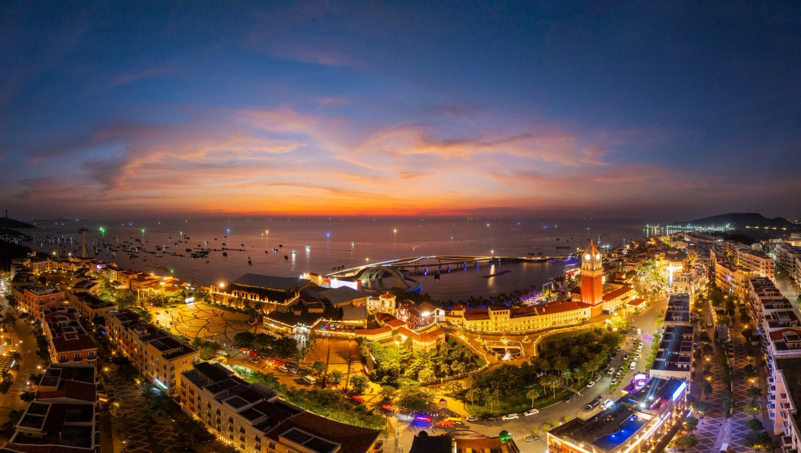 Panoramic view of illuminated streets and the waterfront beneath an evening sky.