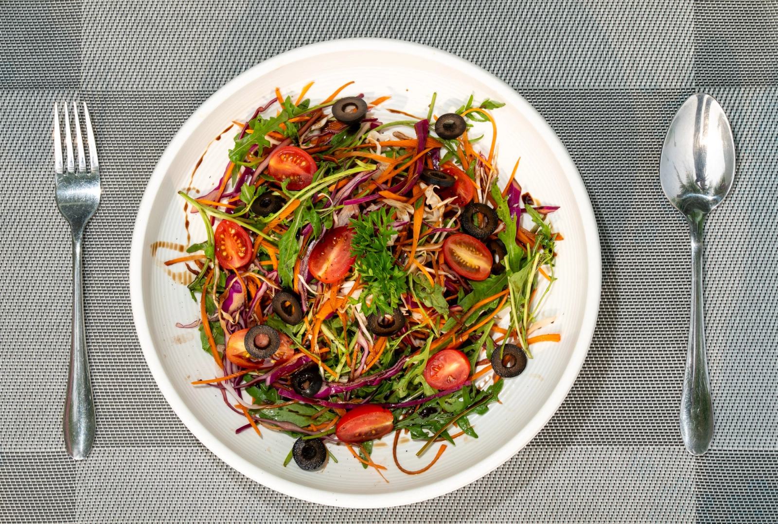 Overhead view of a leafy salad with tomatoes, olives and colourful vegetable strips.
