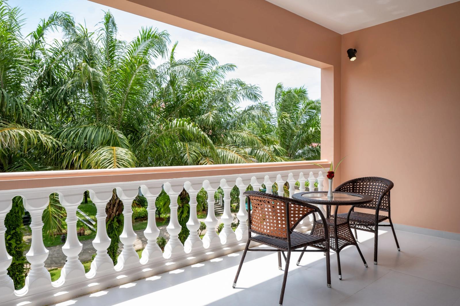Balcony with a round table and two chairs overlooking palm trees.