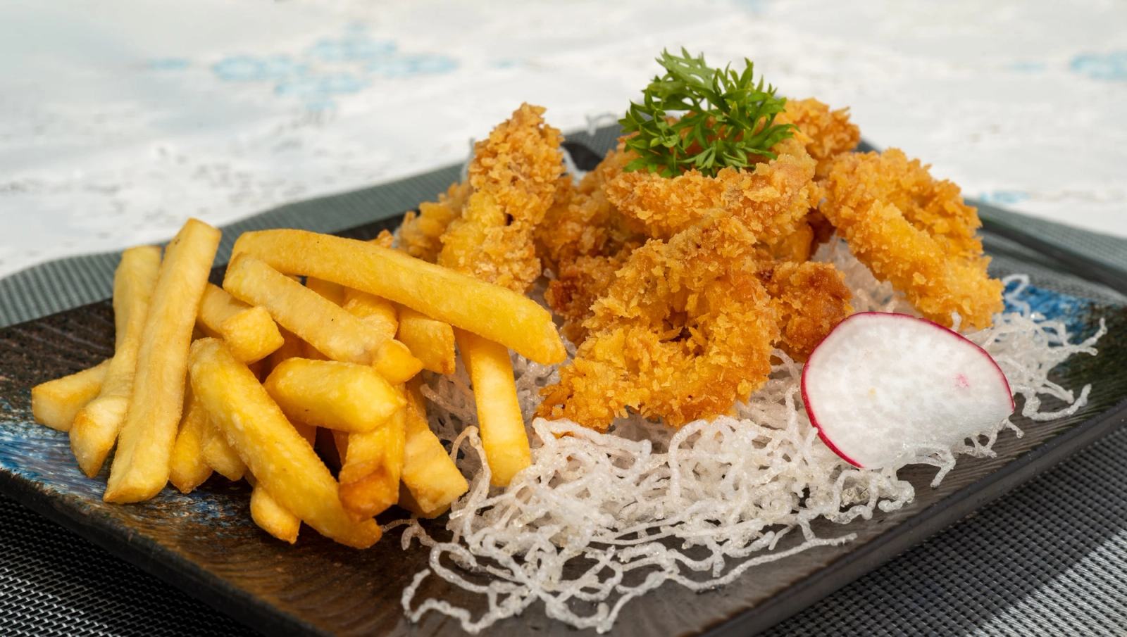 Golden breaded rings and fries served on a dark rectangular plate.