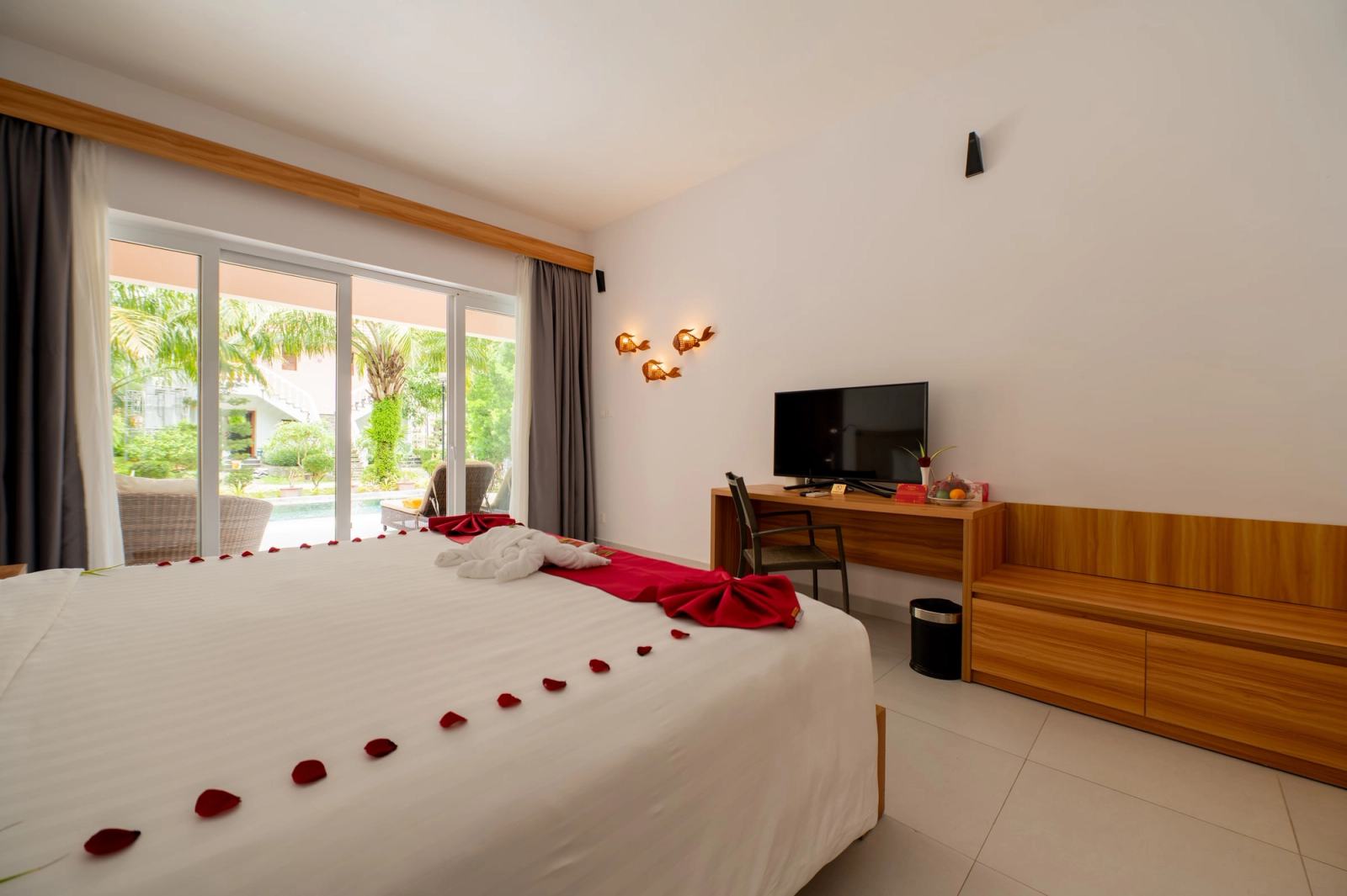 Bedroom with white bedding, red towel decorations and glass doors opening towards greenery.