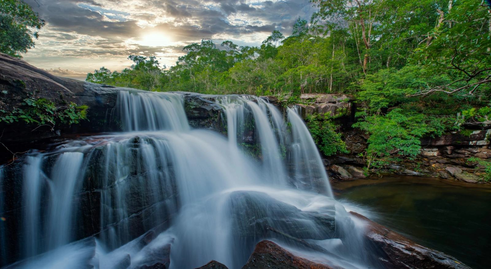 Water cascading over broad rocky ledges surrounded by forest.