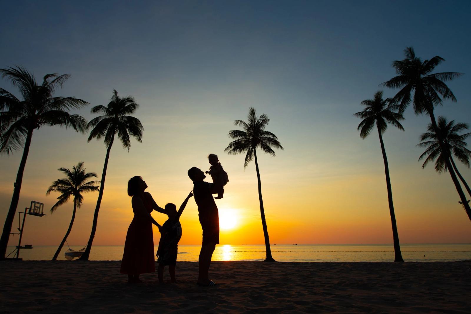 Silhouettes of a family with children beneath palm trees at sunset.