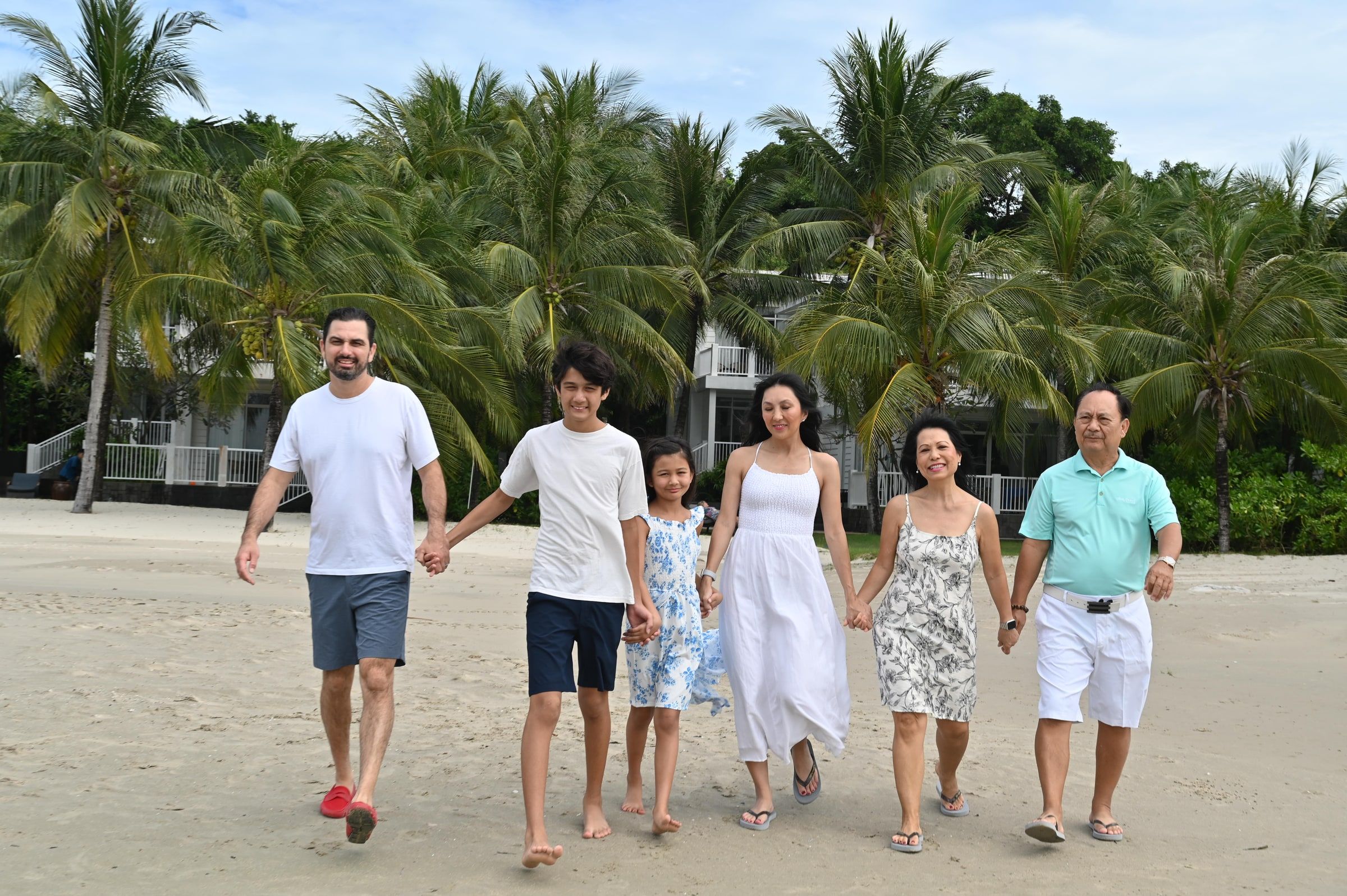 Family members walking hand in hand along a beach in front of palm trees.