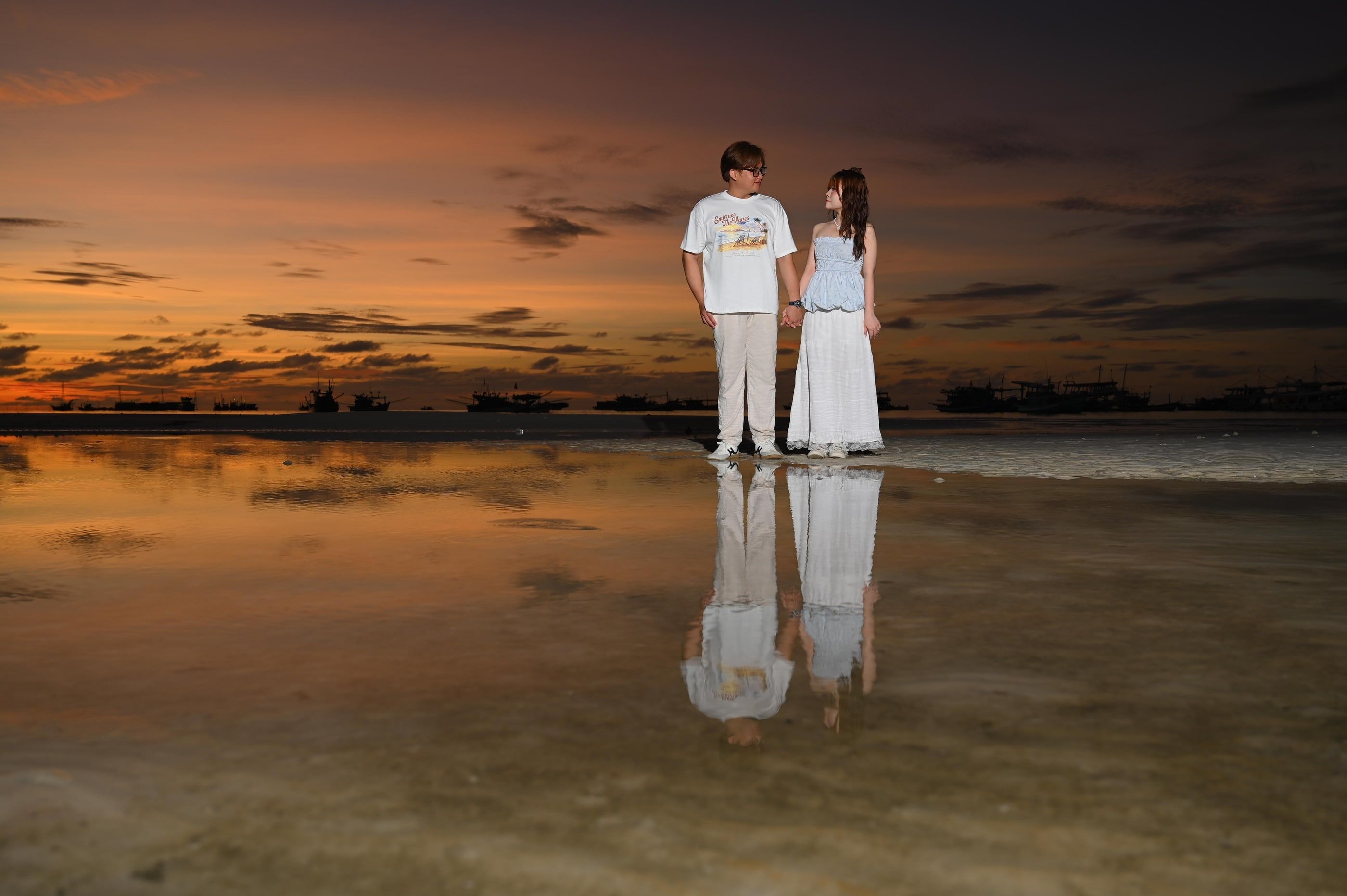 A couple reflected in wet sand at sunset.