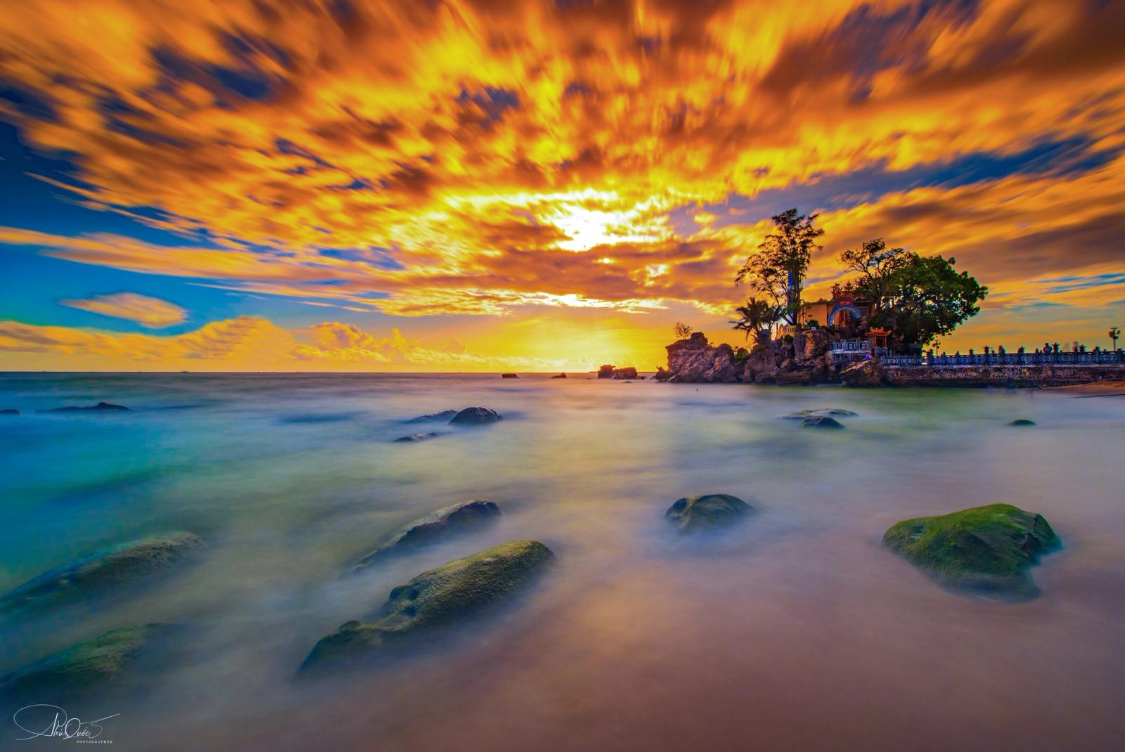 Waves flowing around coastal rocks beneath a golden cloud-filled sky.