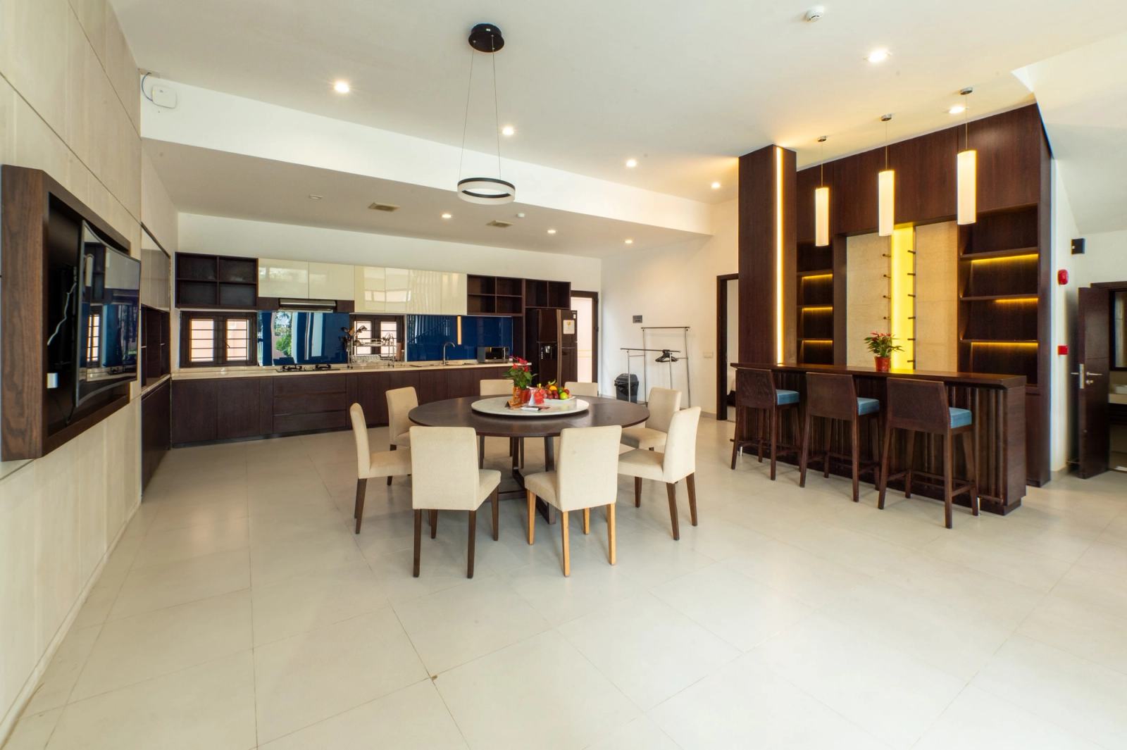 Open-plan dining space with a round table, bar stools and illuminated timber shelving.