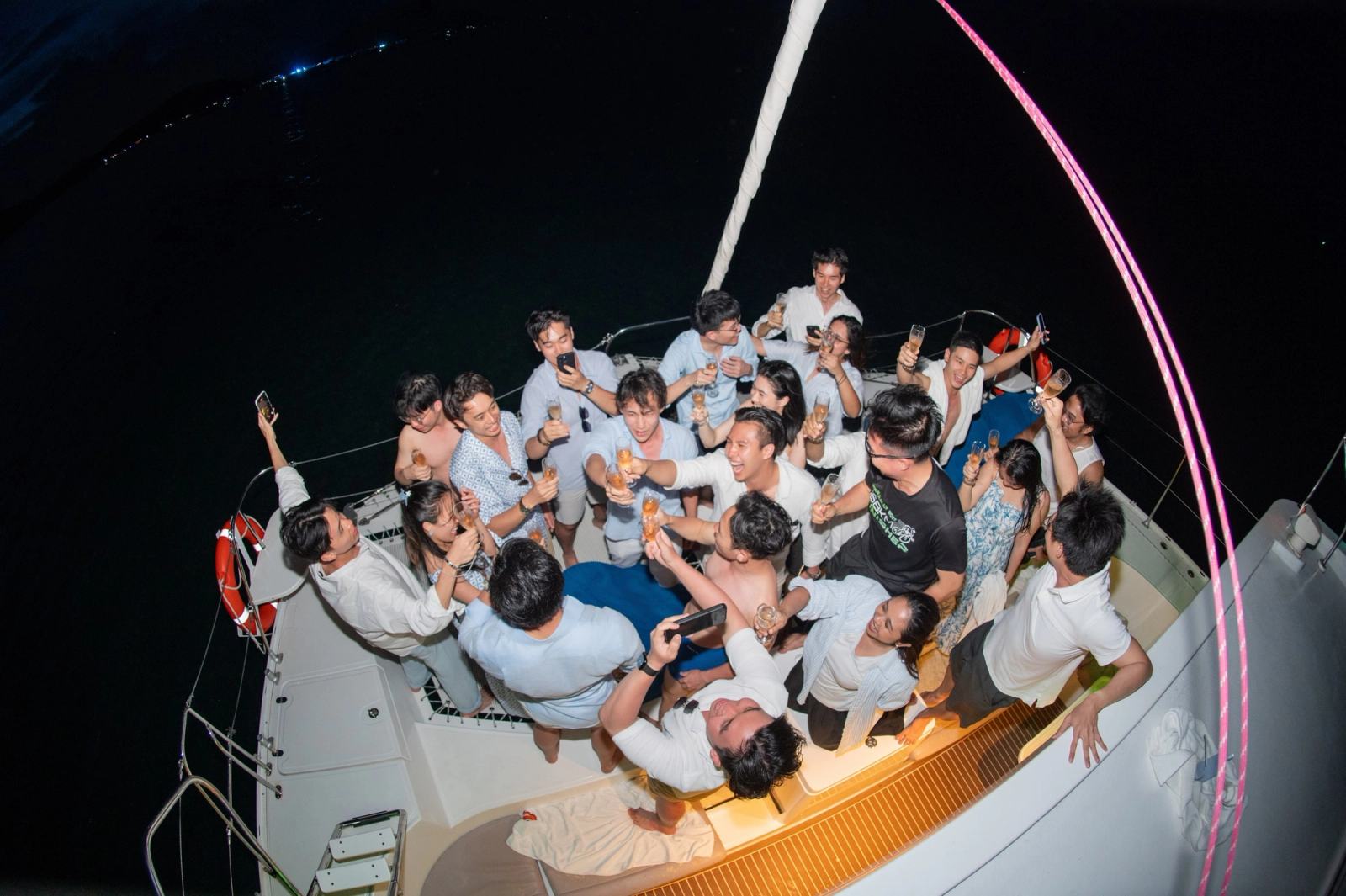 Overhead view of guests raising glasses on a catamaran at night.