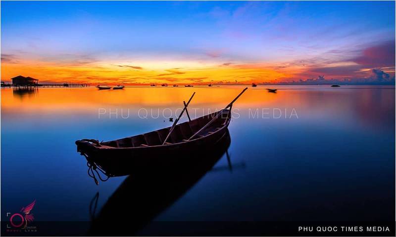 A wooden boat on calm water beneath an orange and blue evening sky
