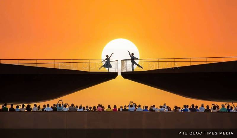 Two performers silhouetted on Kiss Bridge against the setting sun