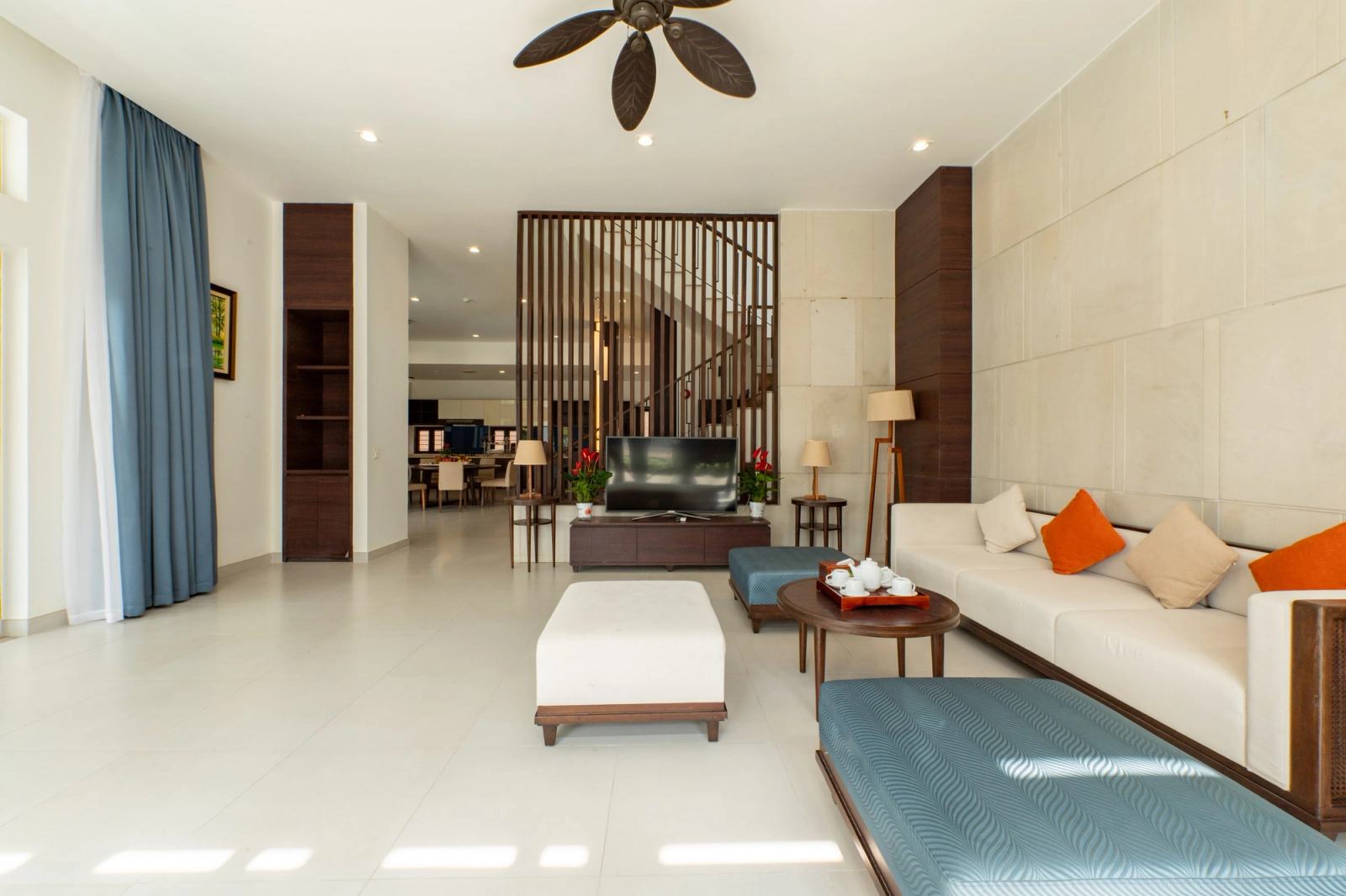 Bright living room with a white sofa, orange cushions and a timber screen beside the staircase.