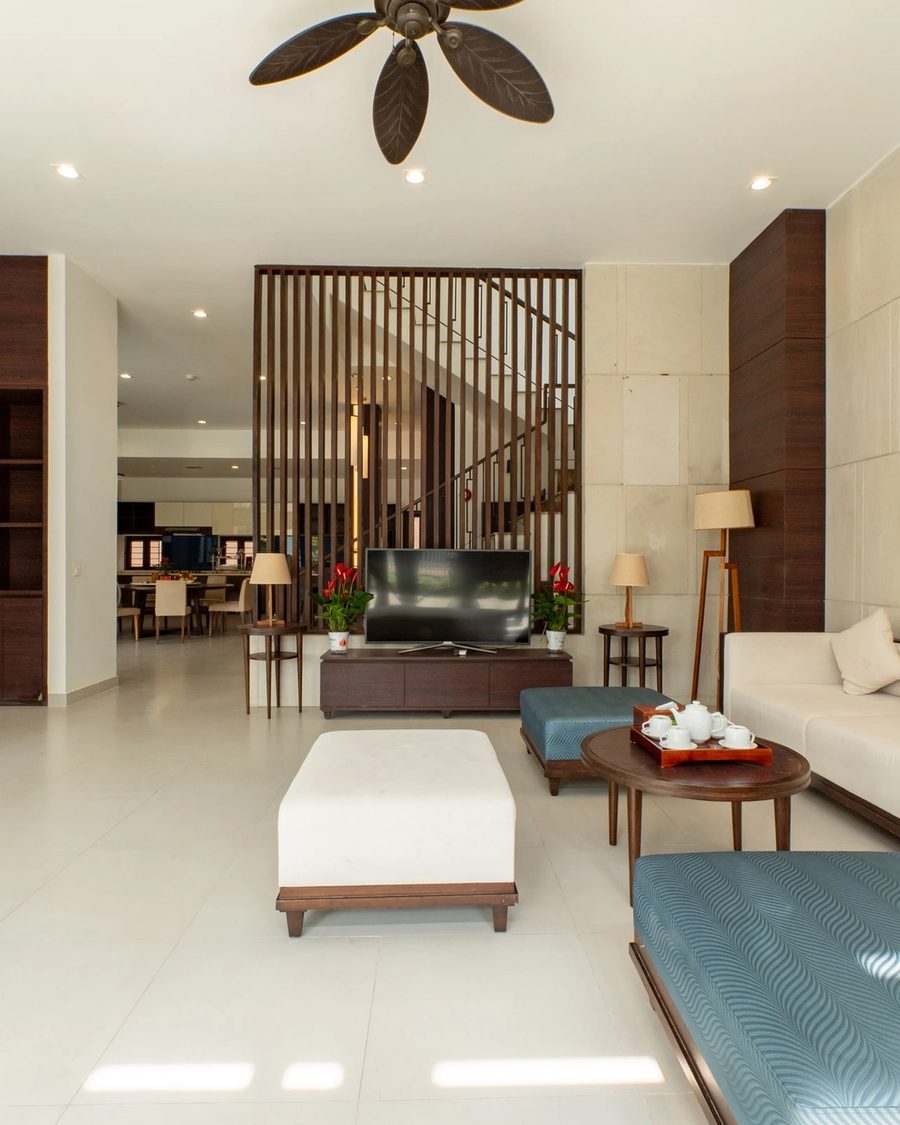 Bright living room with a white sofa, orange cushions and a timber screen beside the staircase.