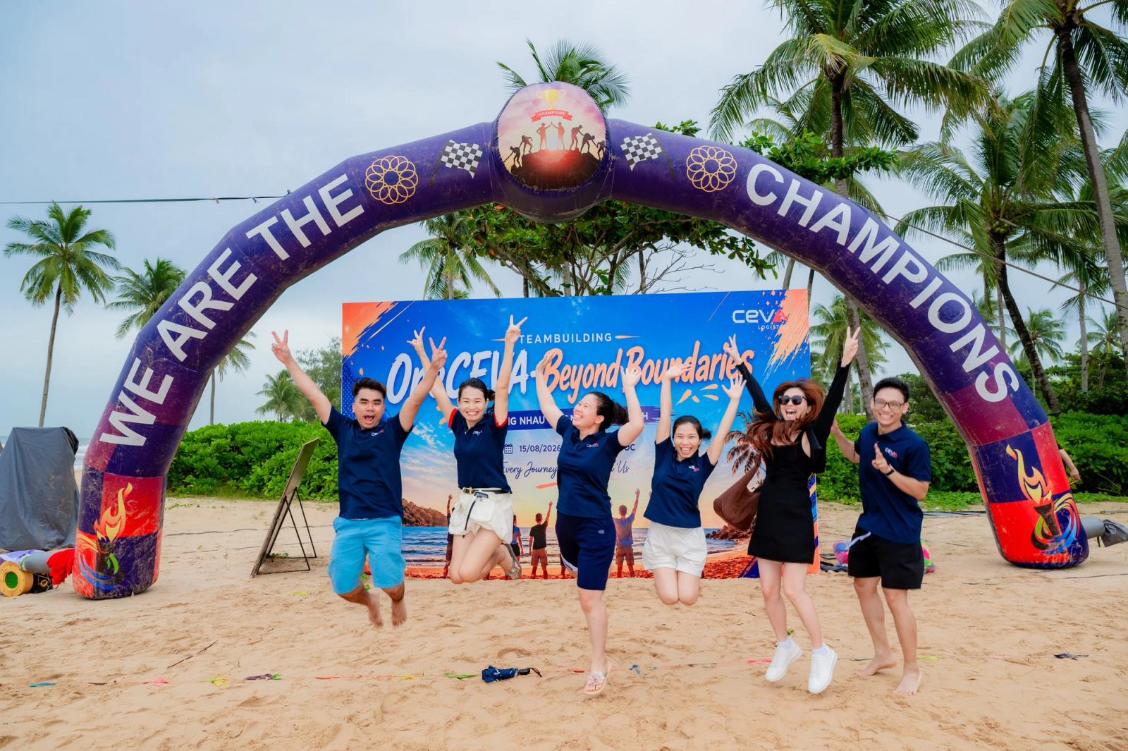 Participants jumping beneath a beach event arch.