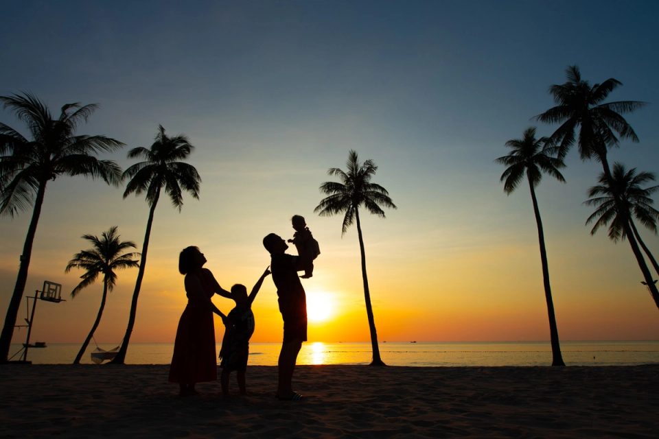 A family silhouetted between palm trees at sunset.