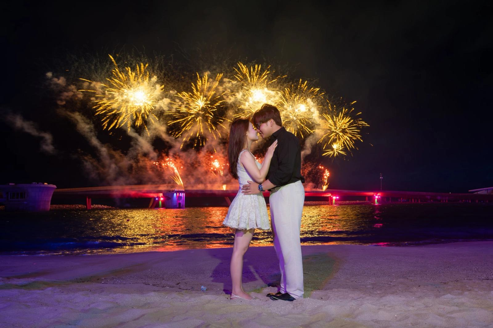 Couple kissing beside the waterfront beneath golden fireworks at night.
