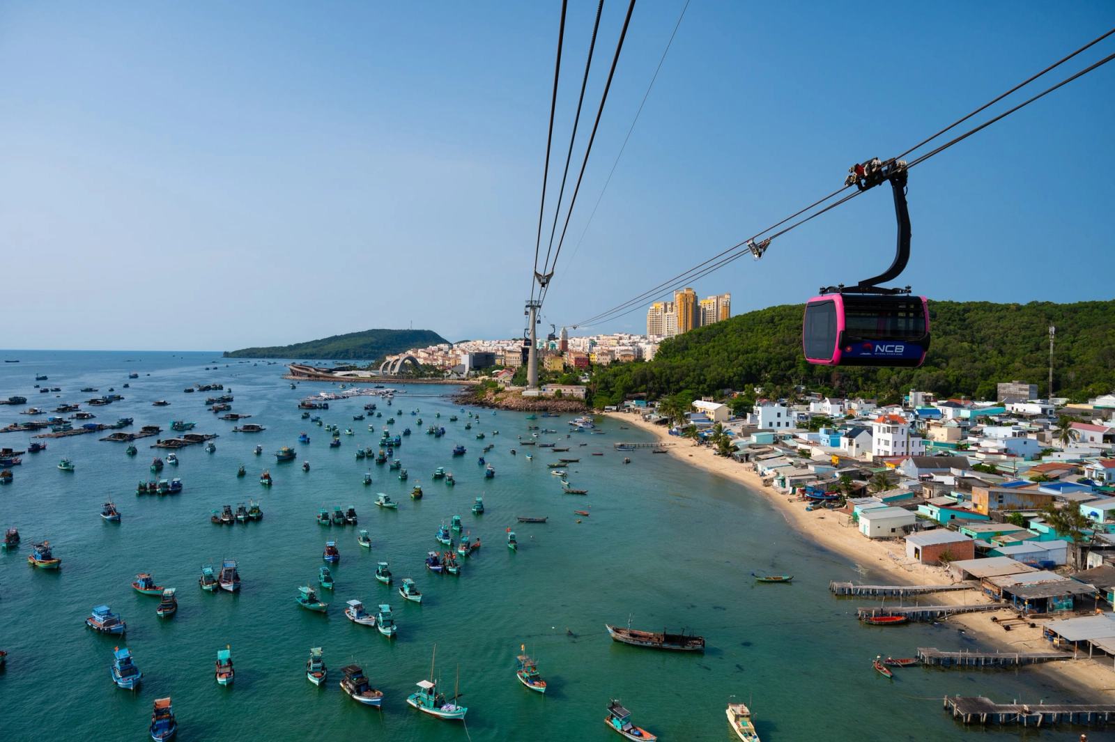 Cable car cabin above fishing boats and waterfront buildings.