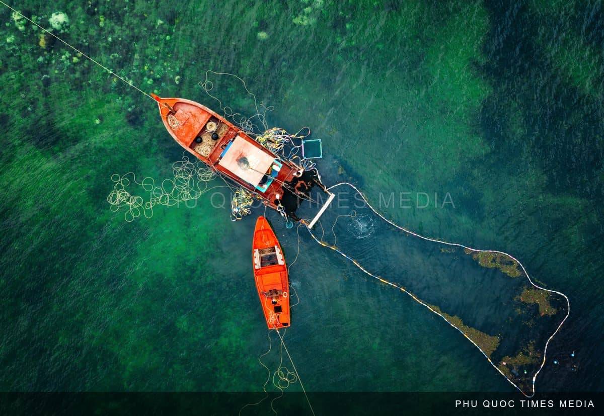 Two orange fishing boats beside a net in green water, photographed from above