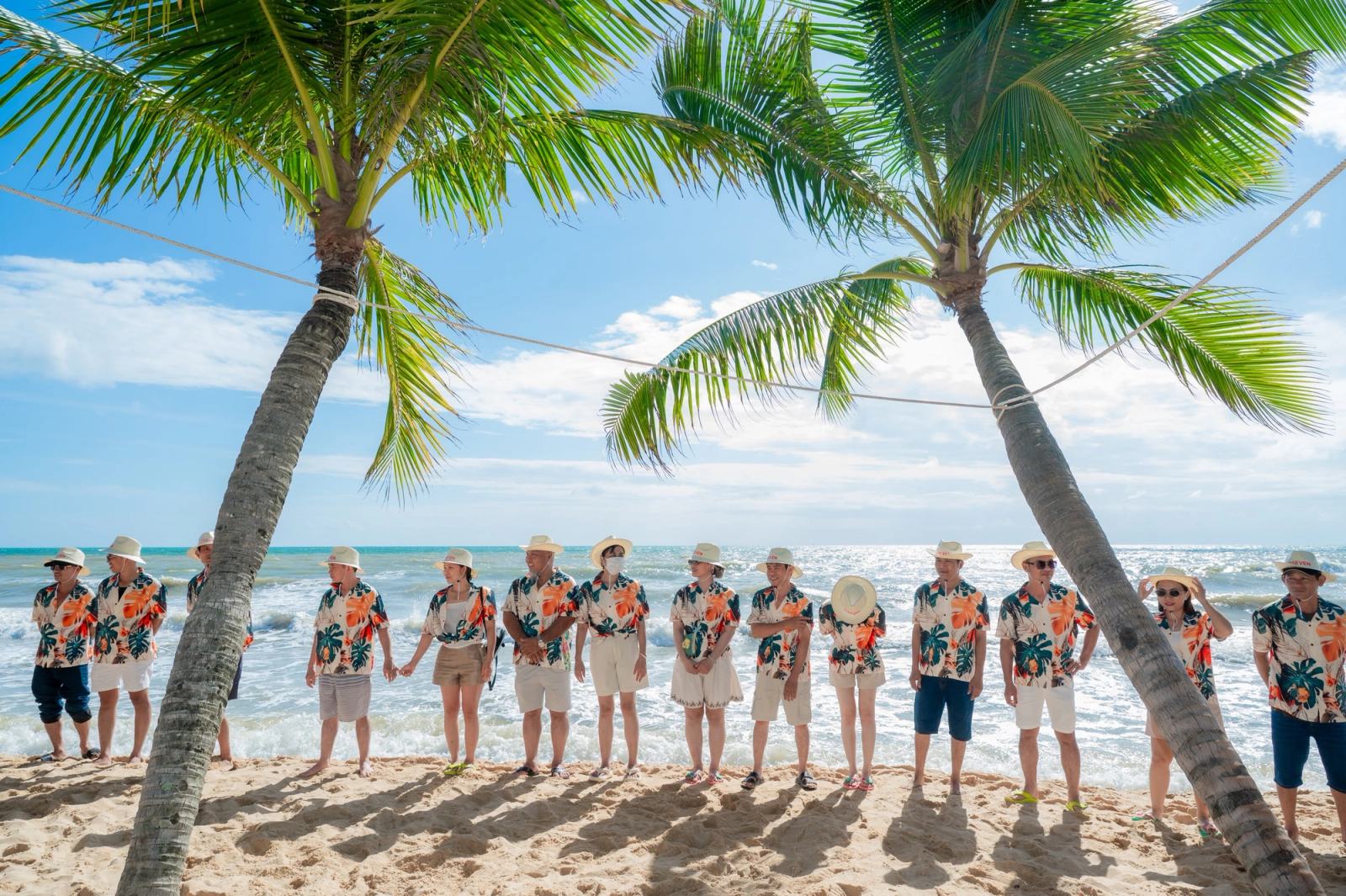 Participants in floral shirts standing together on a palm-lined beach.