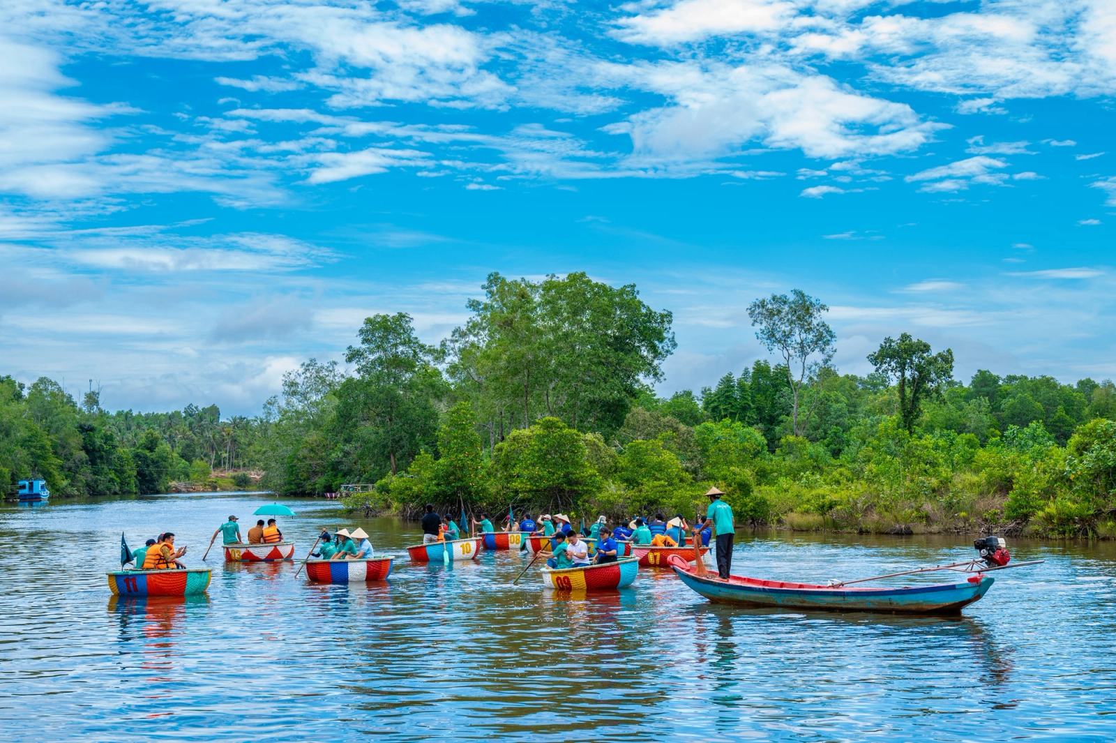 A group in colourful boats on the Cua Can River beside green riverbanks.