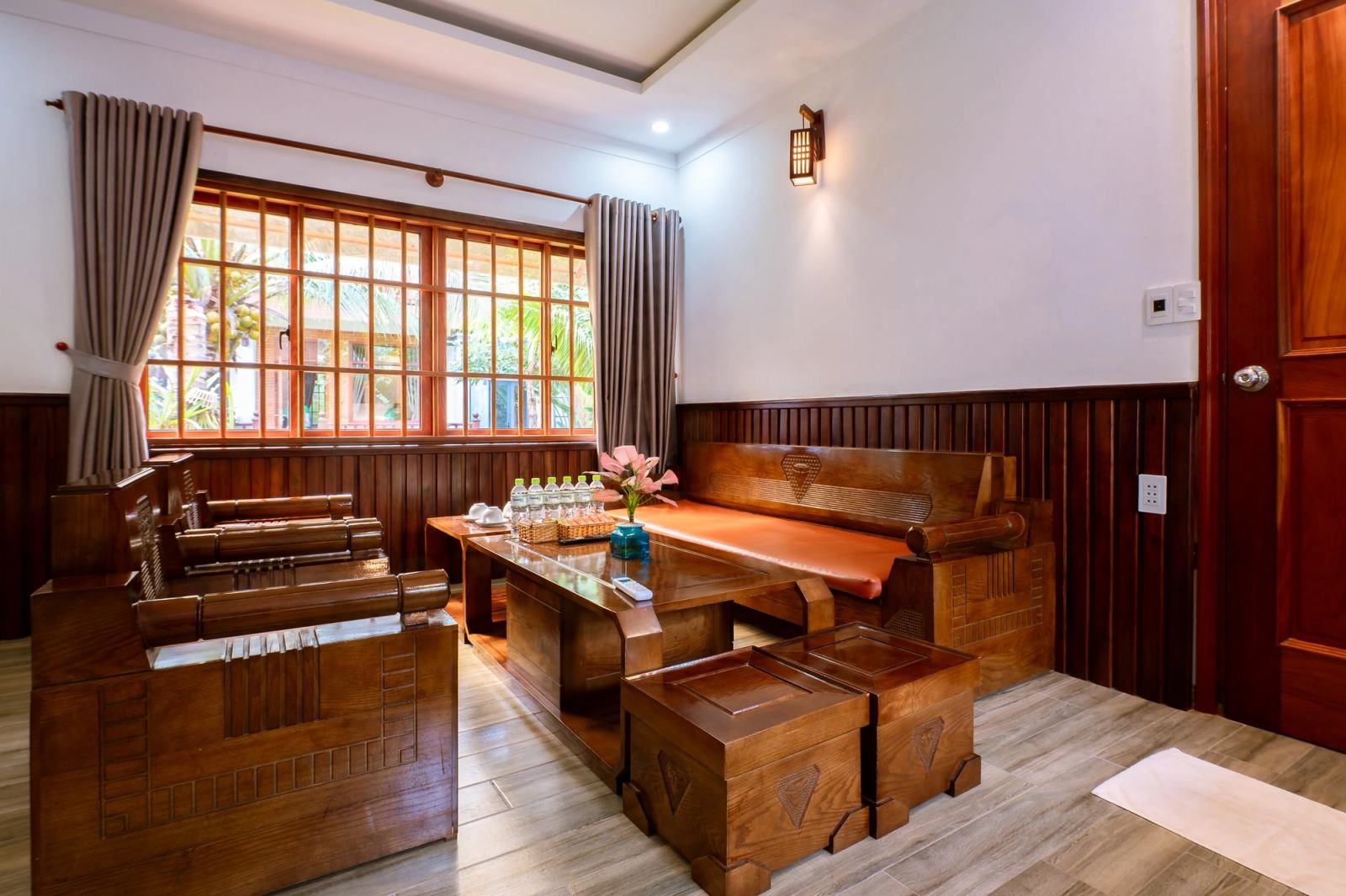Timber seating and a low table beside a large window in a sunlit lounge.