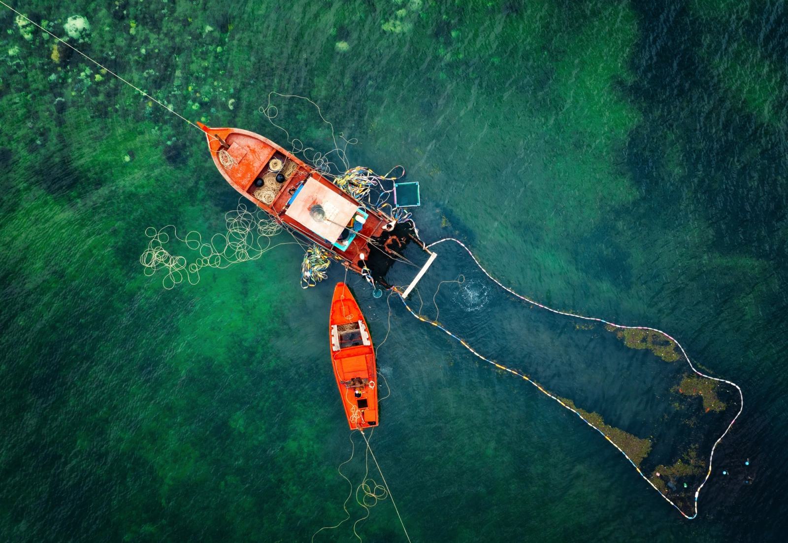 Two fishing boats and nets seen from above in green coastal water.