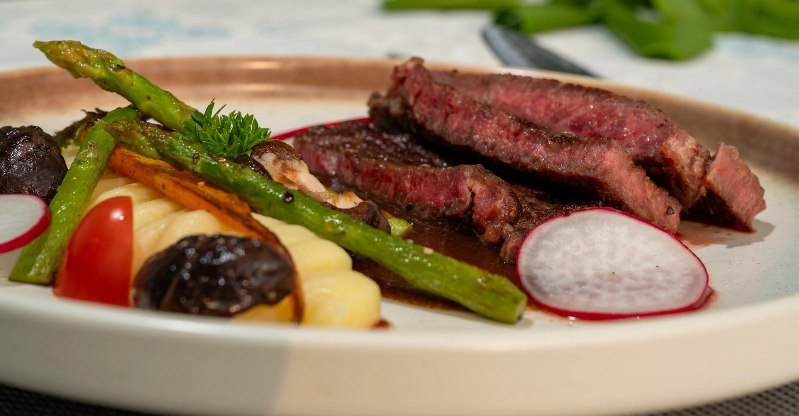 Close-up of sliced steak with a pink centre, asparagus and colourful vegetables.