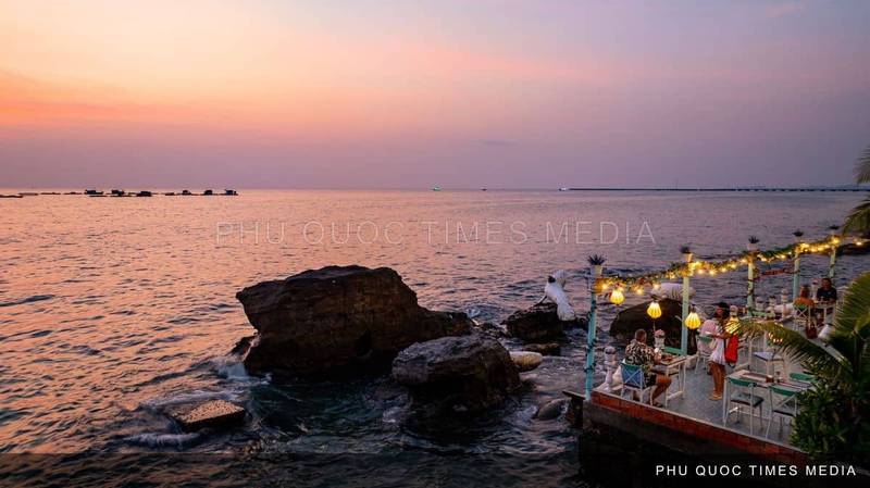 A dining table set on a rocky seafront in soft sunset light