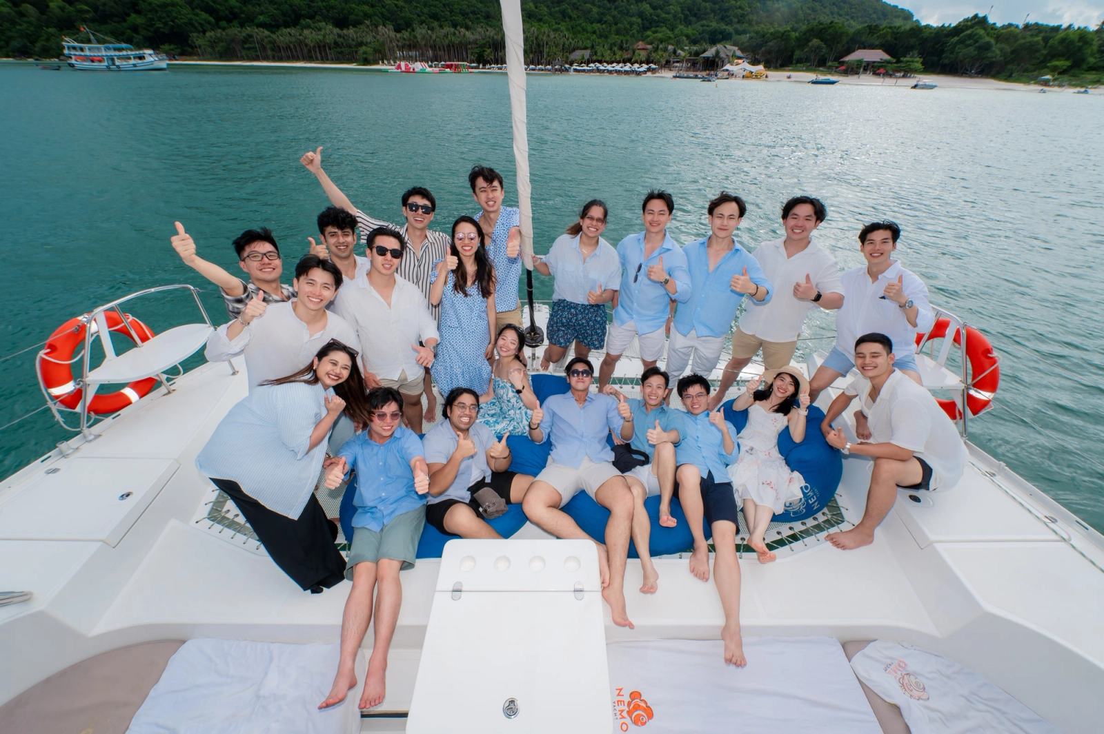 A group posing on the bow of a catamaran with an island beach behind them.