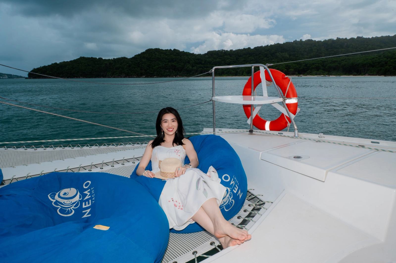A guest relaxing on a blue beanbag on a catamaran beside calm water.