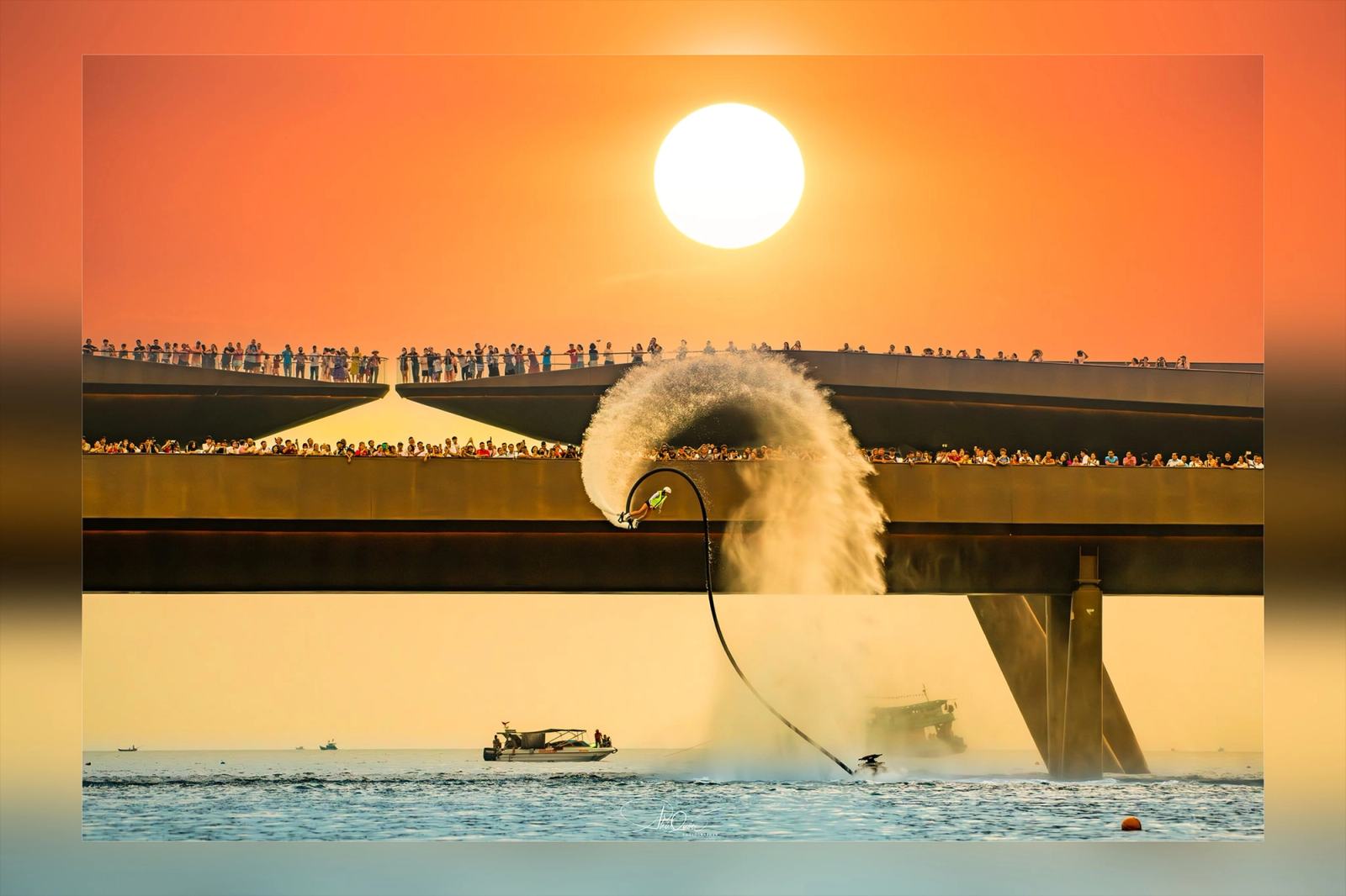 A water-powered performer creating a curved spray beneath the setting sun beside Kiss Bridge.
