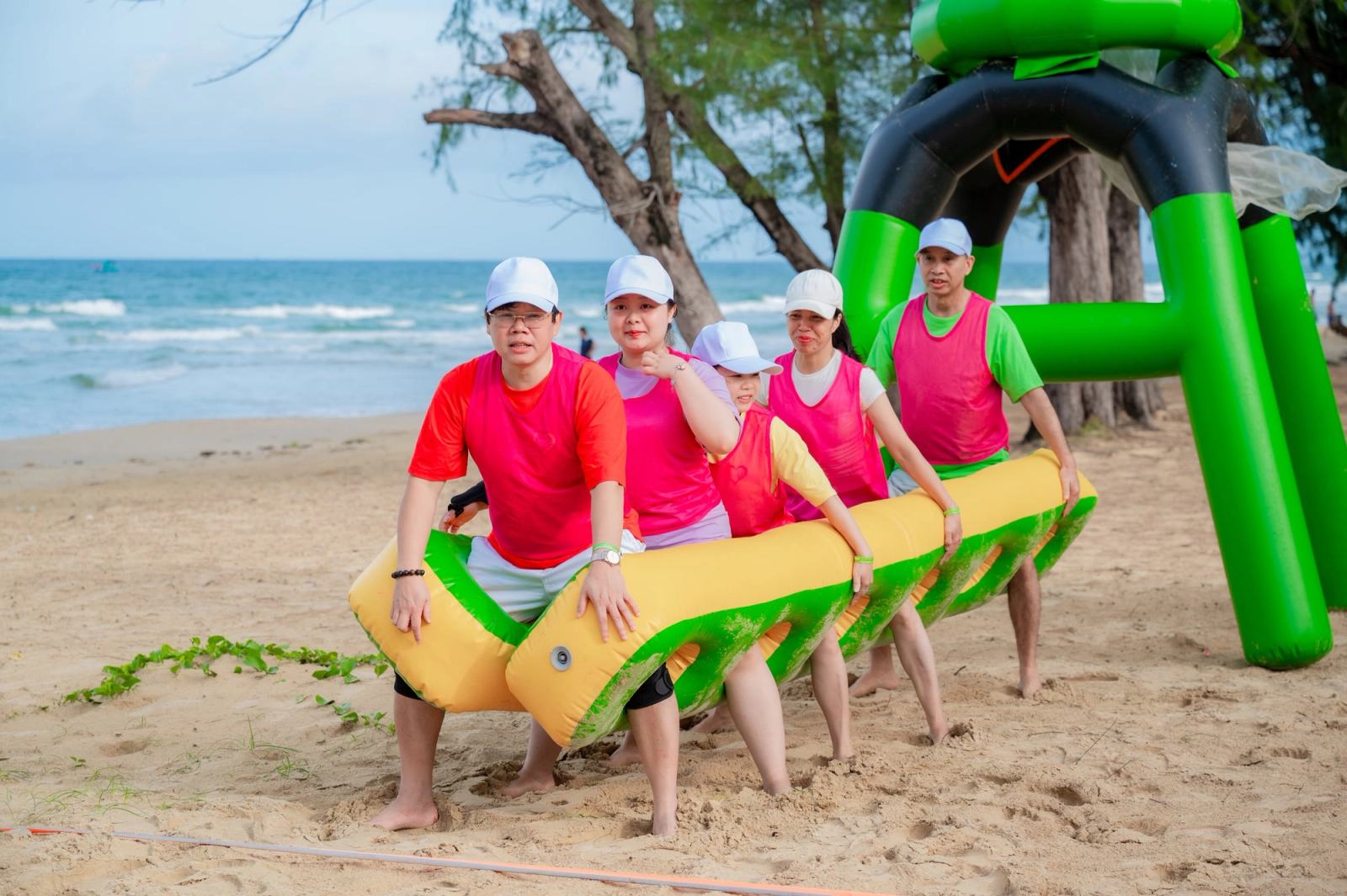 A team carrying a long inflatable prop during a beach game.