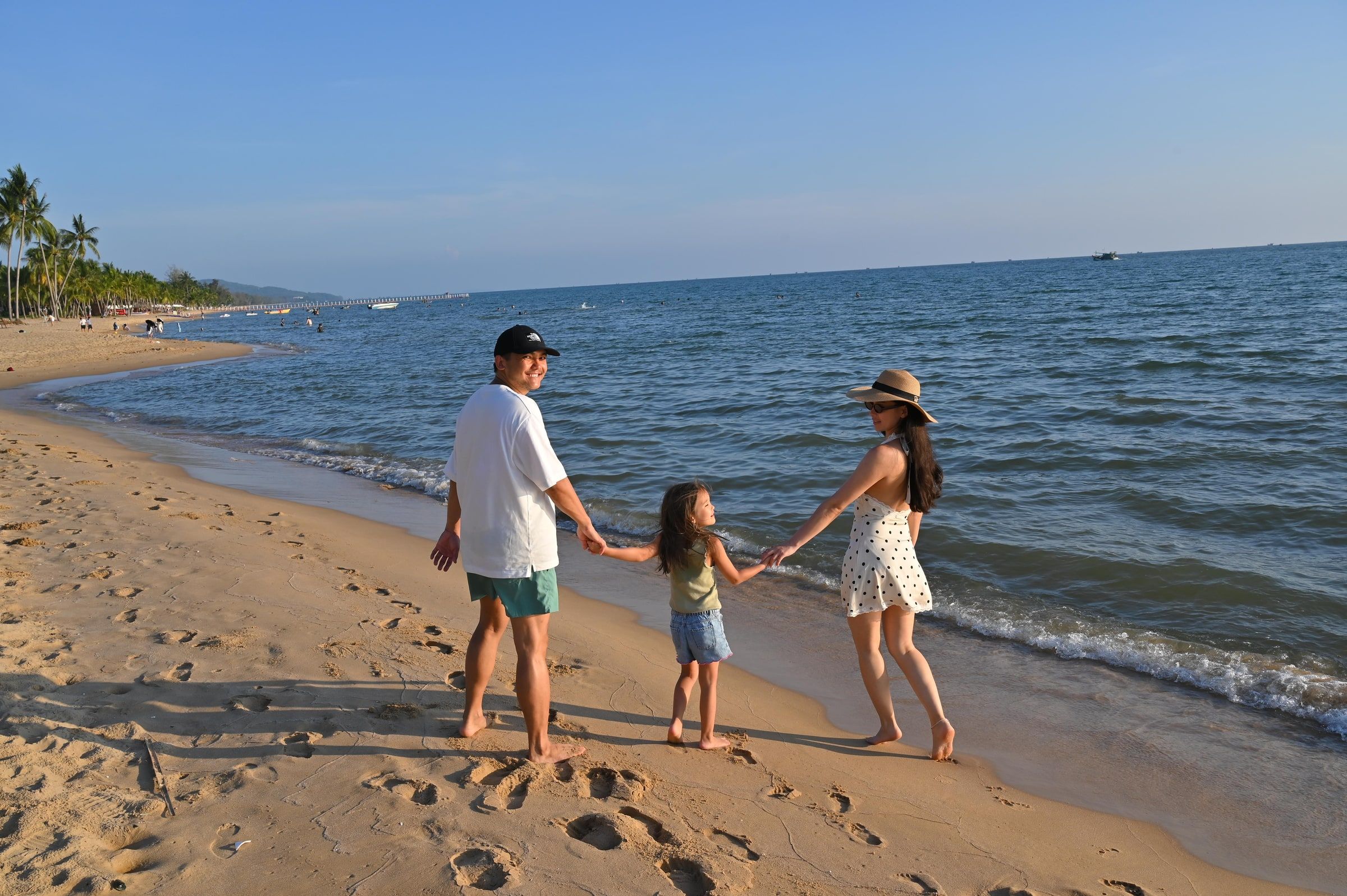 Parents and their daughter holding hands on a sandy beach, seen from behind.