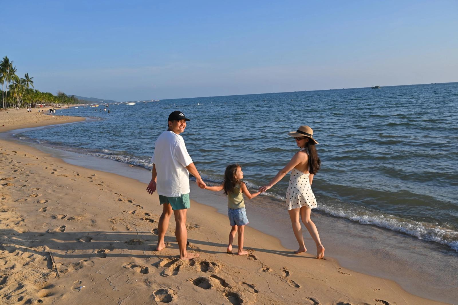 Parents and their daughter holding hands on a sandy beach, seen from behind.