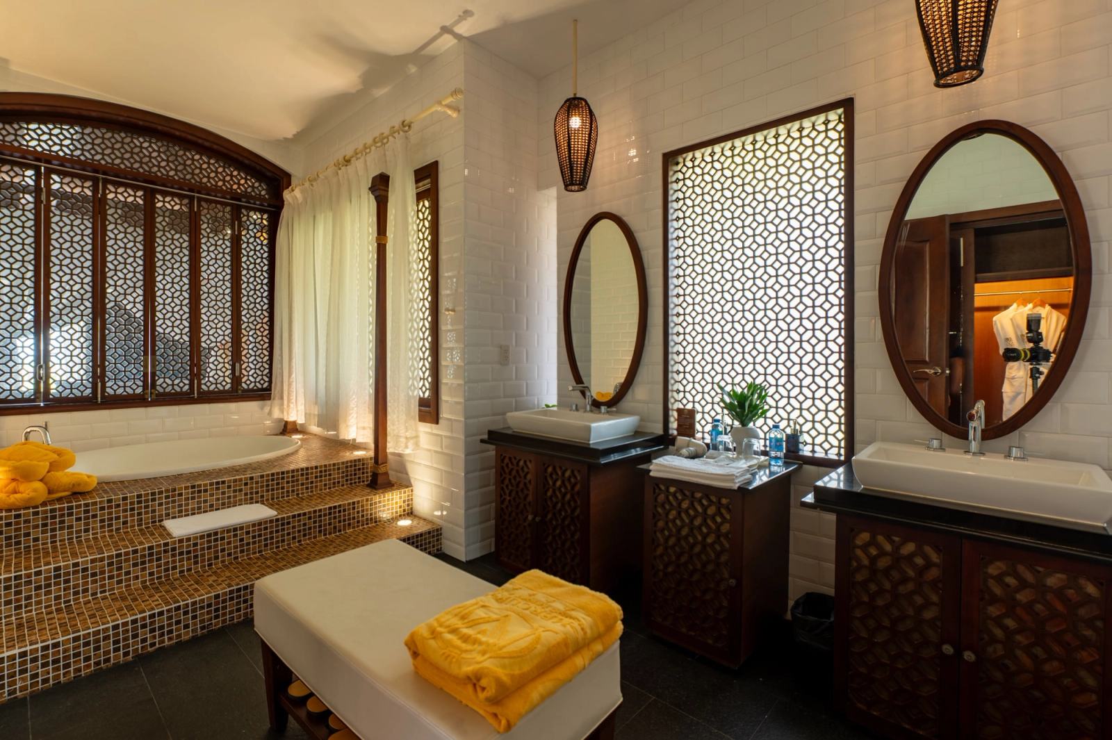 Bathroom with twin washbasins, oval mirrors and a bathtub beside patterned screens.