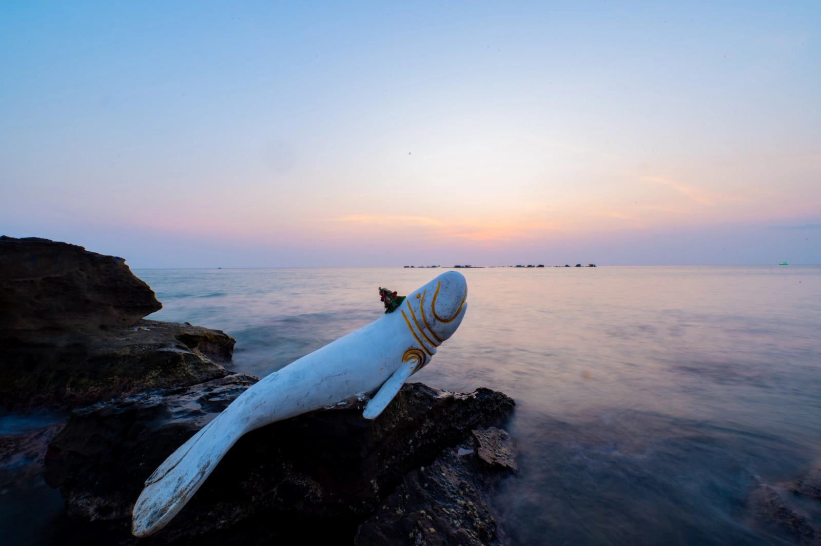 A fish sculpture reaching above coastal rocks at dusk.