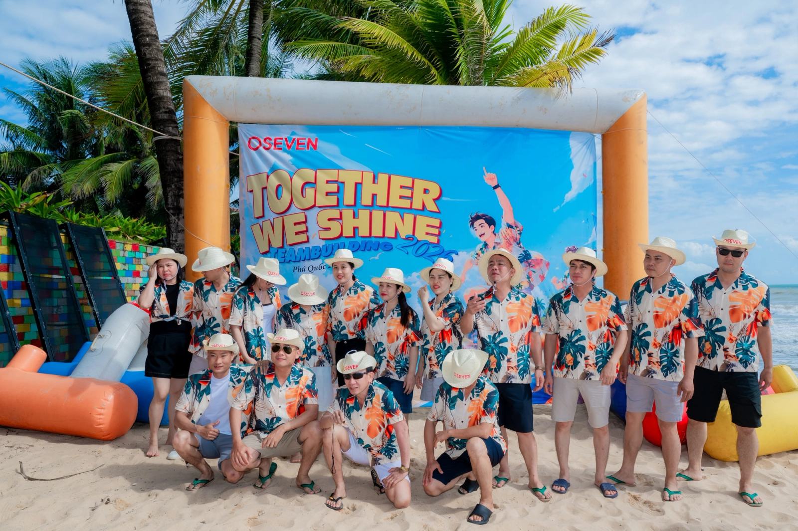 Group in floral shirts gathered in front of an event backdrop among palm trees.