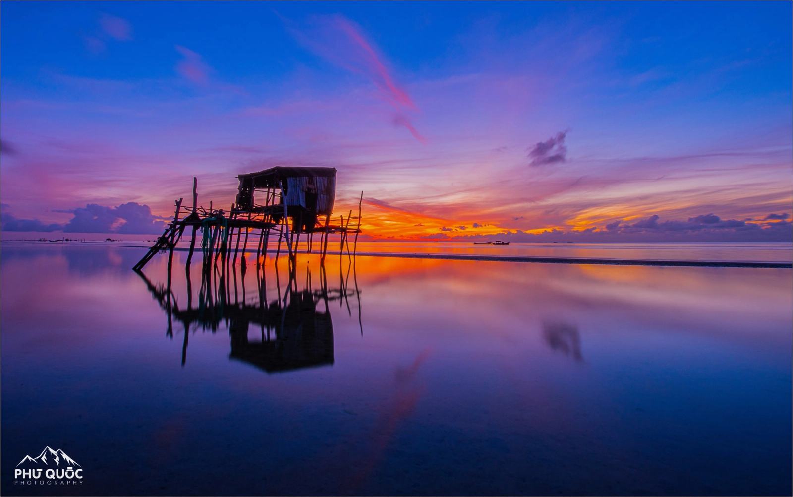 A stilt hut reflected in calm water beneath a pink and blue evening sky.
