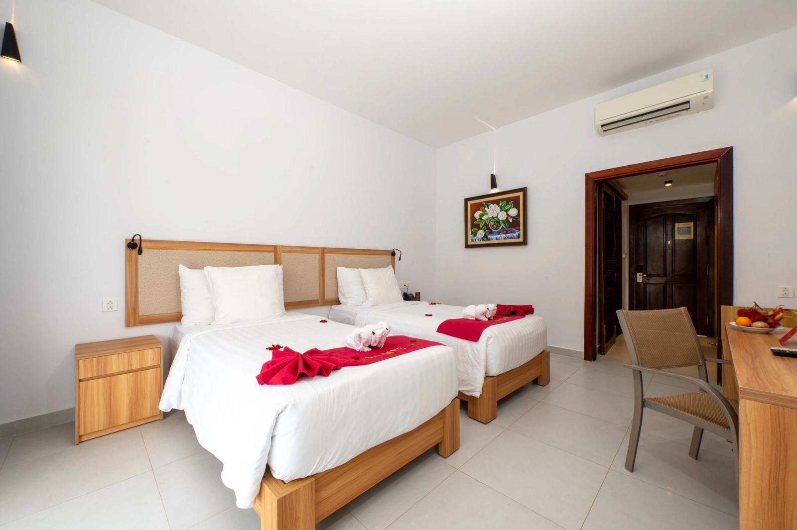 Twin bedroom with timber headboards, white bedding and red towel decorations.