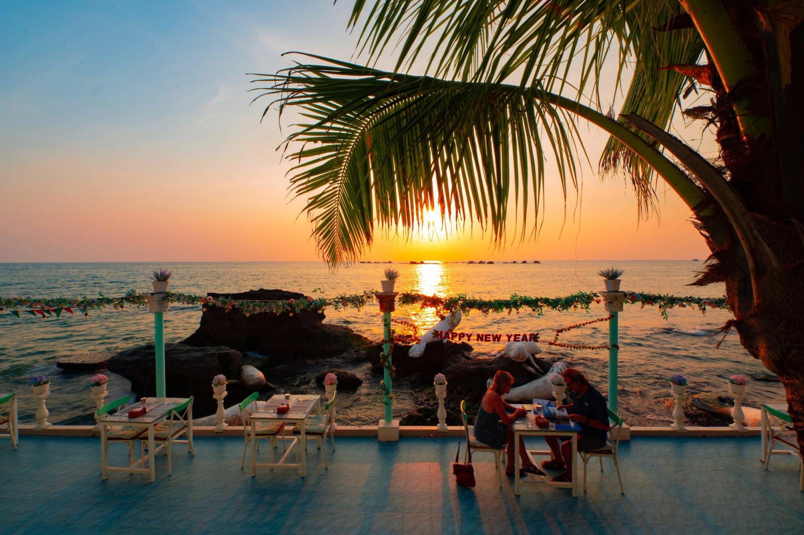 Sunset framed by palm leaves above the seafront dining terrace.